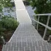 A metal ramp with railings leads down to an aluminum dock over a body of water, surrounded by green foliage and trees—classic of Maine Docks.