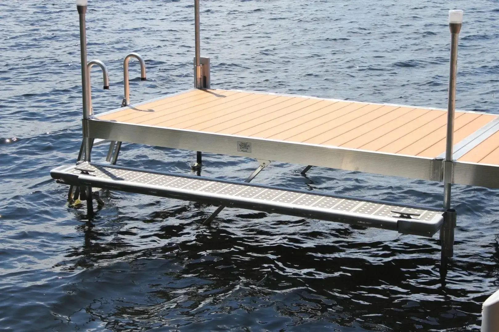 A floating Maine Dock with a tan deck and metal frame extends over rippling water, featuring Boarding Steps attached at the end.