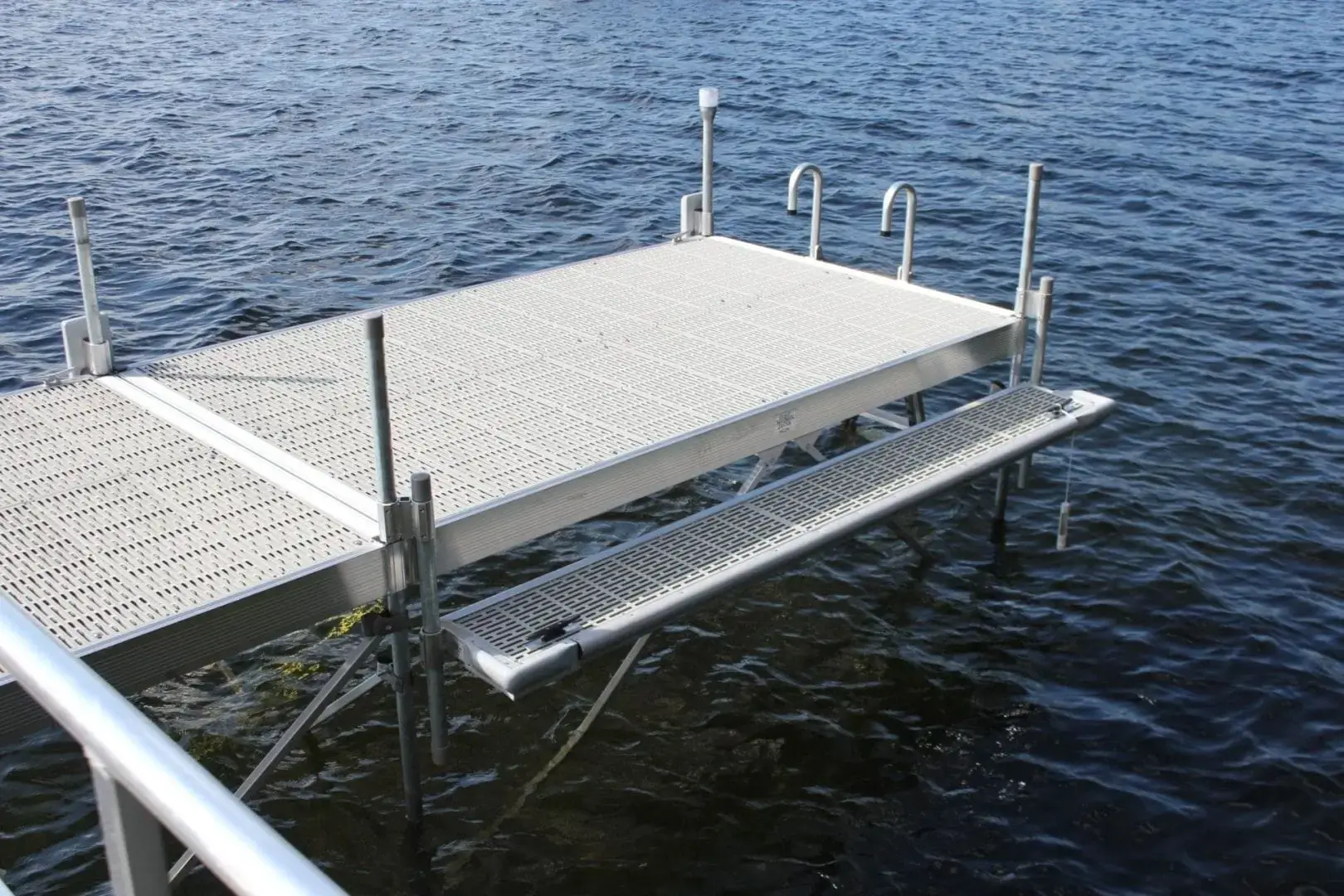 The Boarding Steps by Great Northern Docks extends over the water with a ladder, supported by posts and featuring a bench on one side.