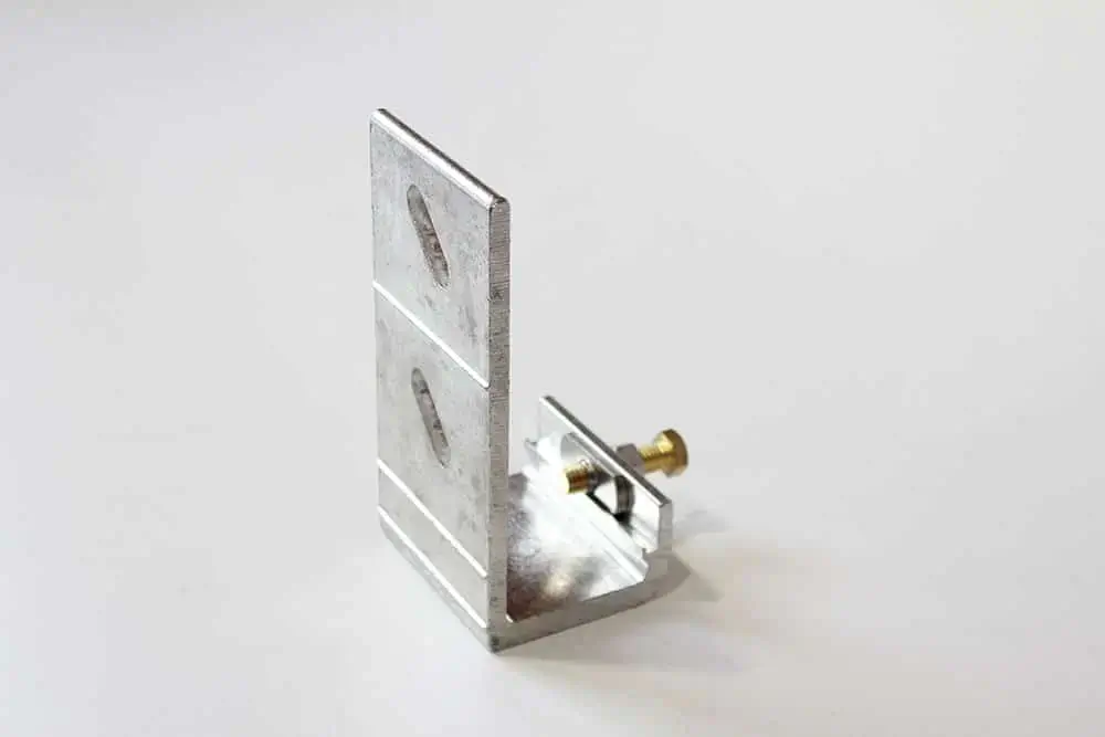 A metal L-bracket with slotted holes and a bolt, used for mounting or supporting objects on wood docks, placed on a white surface.