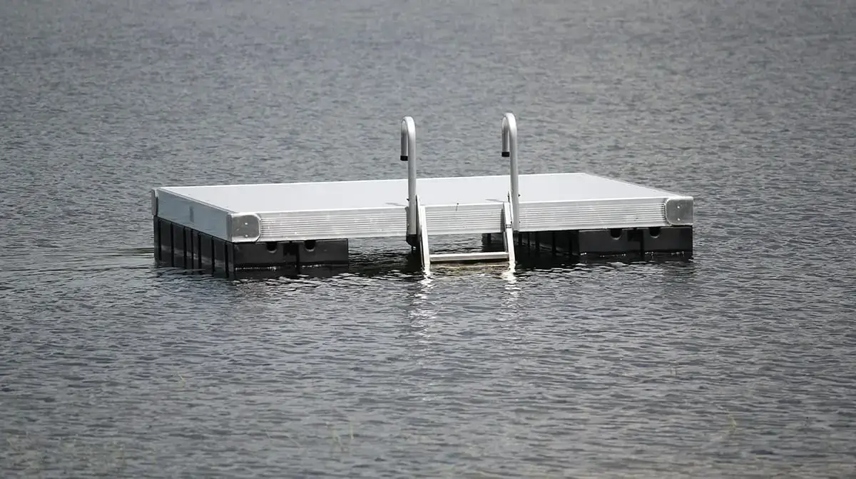 A Maine Docks Swim Raft with a ladder floats on calm water, anchored and empty, showcasing the quality craftsmanship of their products.