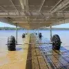 View from under a Roller Dock with large black wheels over clear shallow water, extending toward a lake, with Maine Docks and trees in the background.