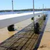 The Roller Dock from Great Northern Docks extends on wheels into a clear, shallow lake with a sandy bottom and trees lining the distant shore under a blue sky.