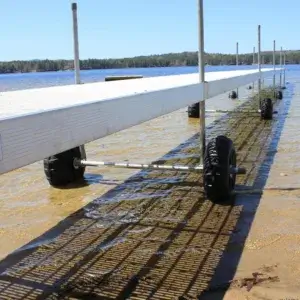 The Roller Dock from Great Northern Docks extends on wheels into a clear, shallow lake with a sandy bottom and trees lining the distant shore under a blue sky.