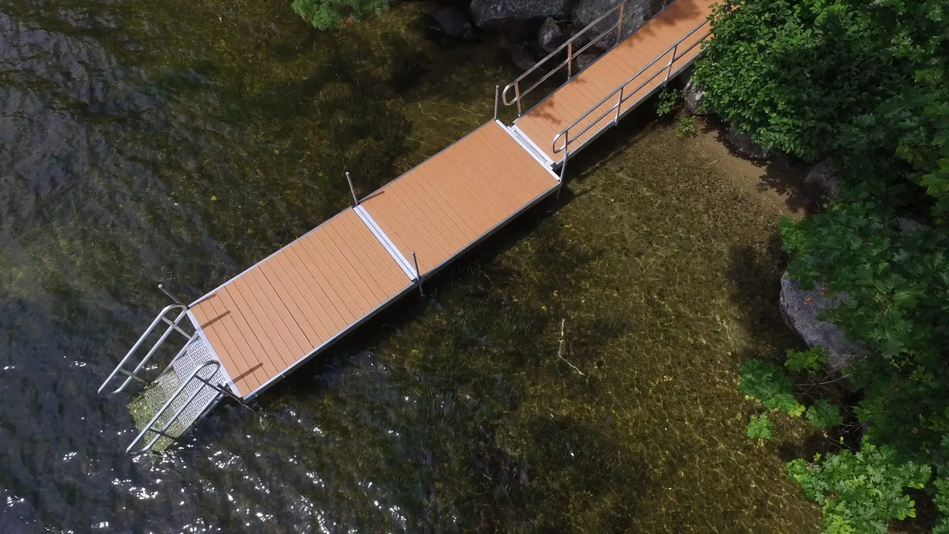 Aerial view of a wooden dock by Great Northern Docks, with metal railings over clear water, surrounded by lush green vegetation.