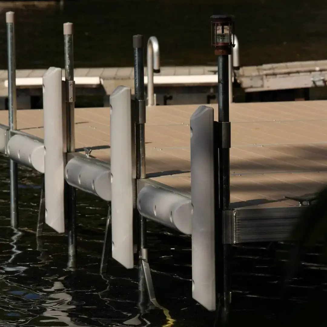 A close-up view of a Great Northern Docks boat dock with white bumpers, metal poles, and a small light fixture, extending over calm water.