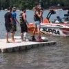 1000SeriesKOW-low Four people stand on a Swim Raft - Connect-A-Dock by a Supra boat on a lake; one holds a wakeboard while others wear life vests.