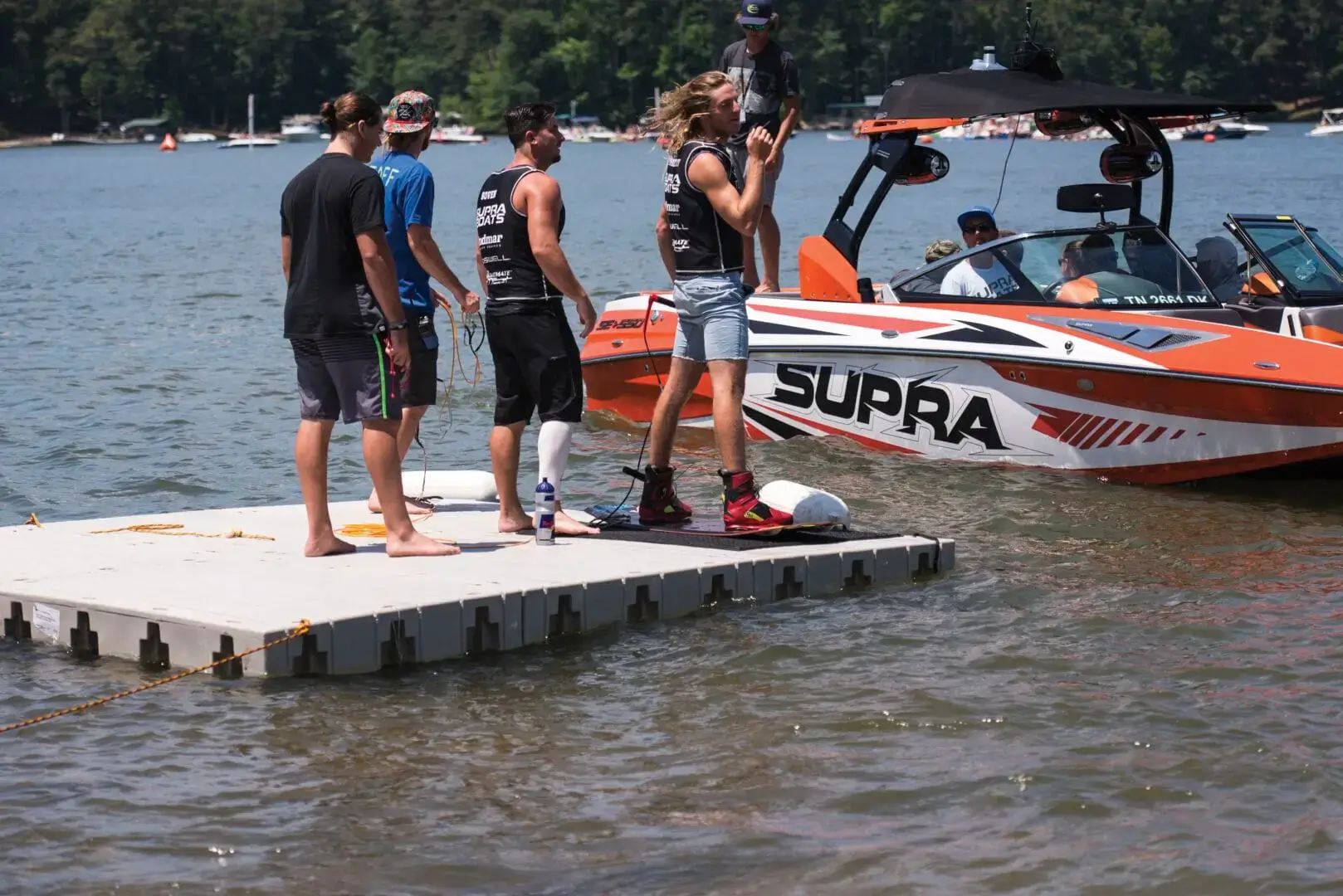 1000SeriesKOW-low Four people stand on a Swim Raft - Connect-A-Dock by a Supra boat on a lake; one holds a wakeboard while others wear life vests.