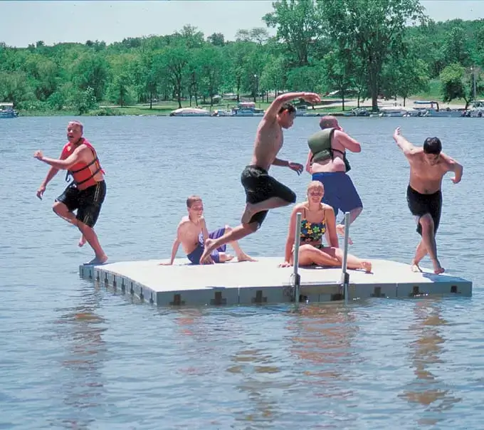 1000Swim-low Six people enjoy a sunny day on a Swim Raft - Connect-A-Dock; some leap into the lake while others relax and smile, surrounded by Maine's scenic trees.