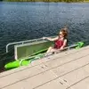 3 A woman in a green kayak uses a Connect-A-Dock Kayak Launch to enter the water, wearing sunglasses and a life jacket on a sunny day.