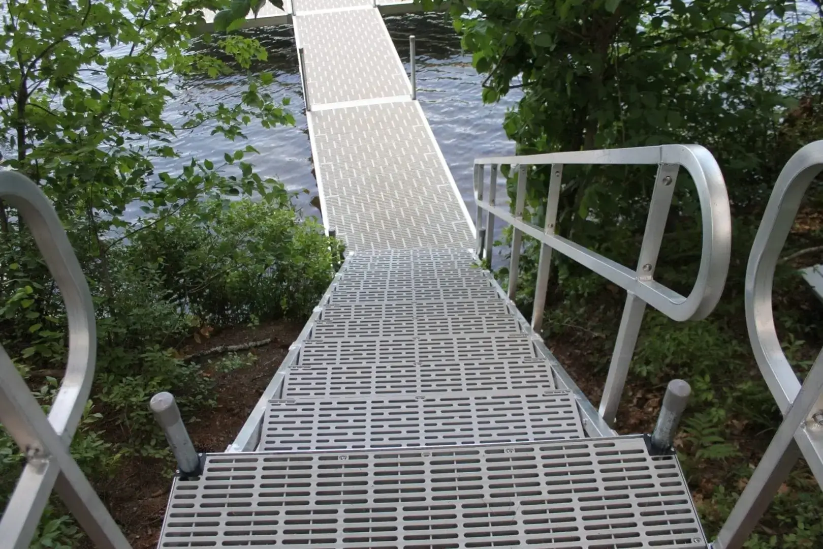 A metal walkway with railings leads down through greenery to a dock extending over a body of water.
