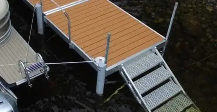 A metal and wood dock extends over dark water, with a metal grated ramp leading down from the dock to the shore.