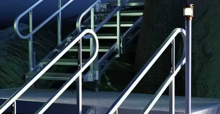 Metal stairs with handrails leading upward, illuminated by a small lamp post; a rock wall is visible beside the stairs.