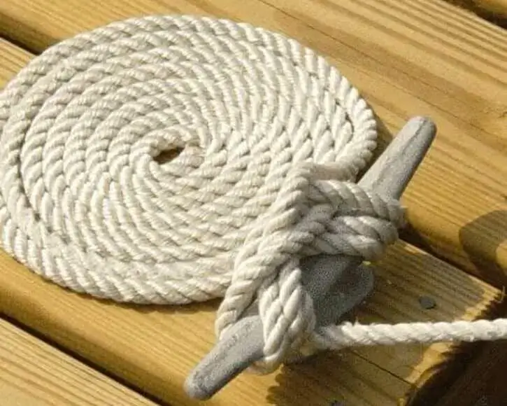 A coiled white rope is neatly tied to a gray cleat on a wooden dock.
