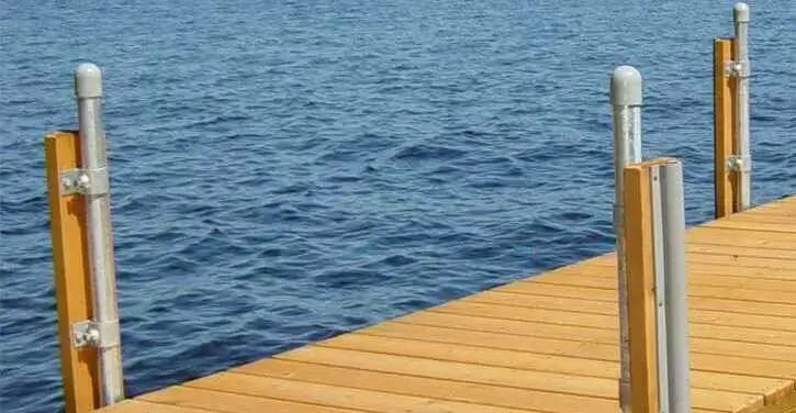 A wooden dock with metal posts extends over calm blue water on a lake.