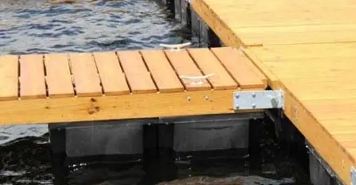 A broken wooden dock with a missing plank connects to a larger dock over choppy water.