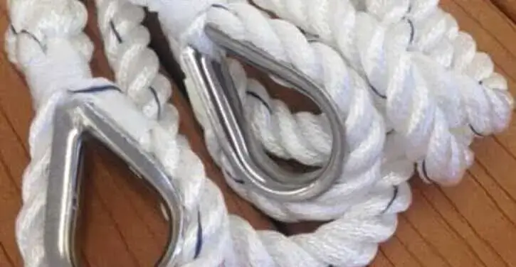 Close-up of two white braided ropes with metal thimbles on a wooden surface.