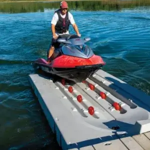 A person rides a red jet ski onto a PWC Port - Connect-A-Dock, surrounded by calm water and greenery.